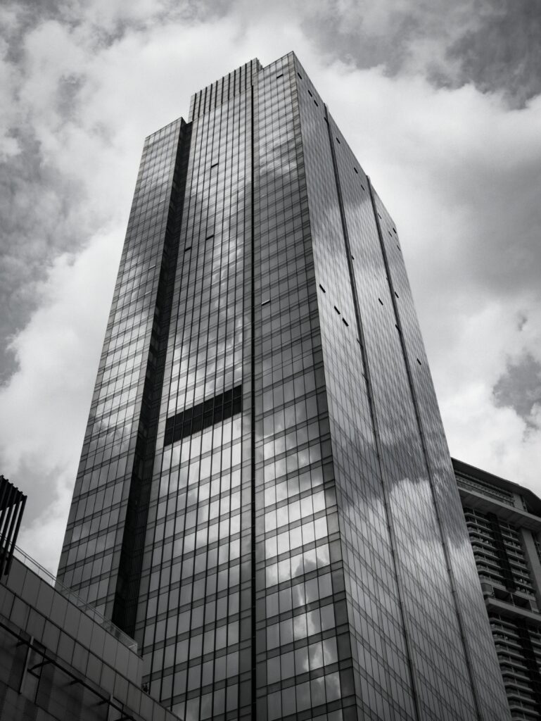 Dramatic black and white photo of a modern skyscraper reflecting clouds on its glass facade.