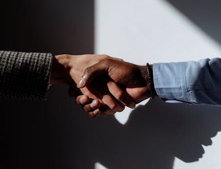 Close-up of two hands shaking under strong lighting, casting dramatic shadows.